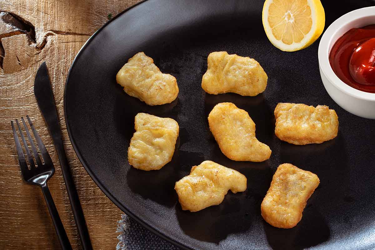 Hähnchennuggets im Backteig, gebraten, auf schwarzem Teller serviert, mit Besteck und etwas Beilage