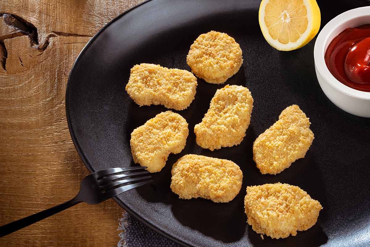 Hähnchennuggets paniert und gebraten, auf schwarzem Teller serviert, mit Besteck und etwas Beilage